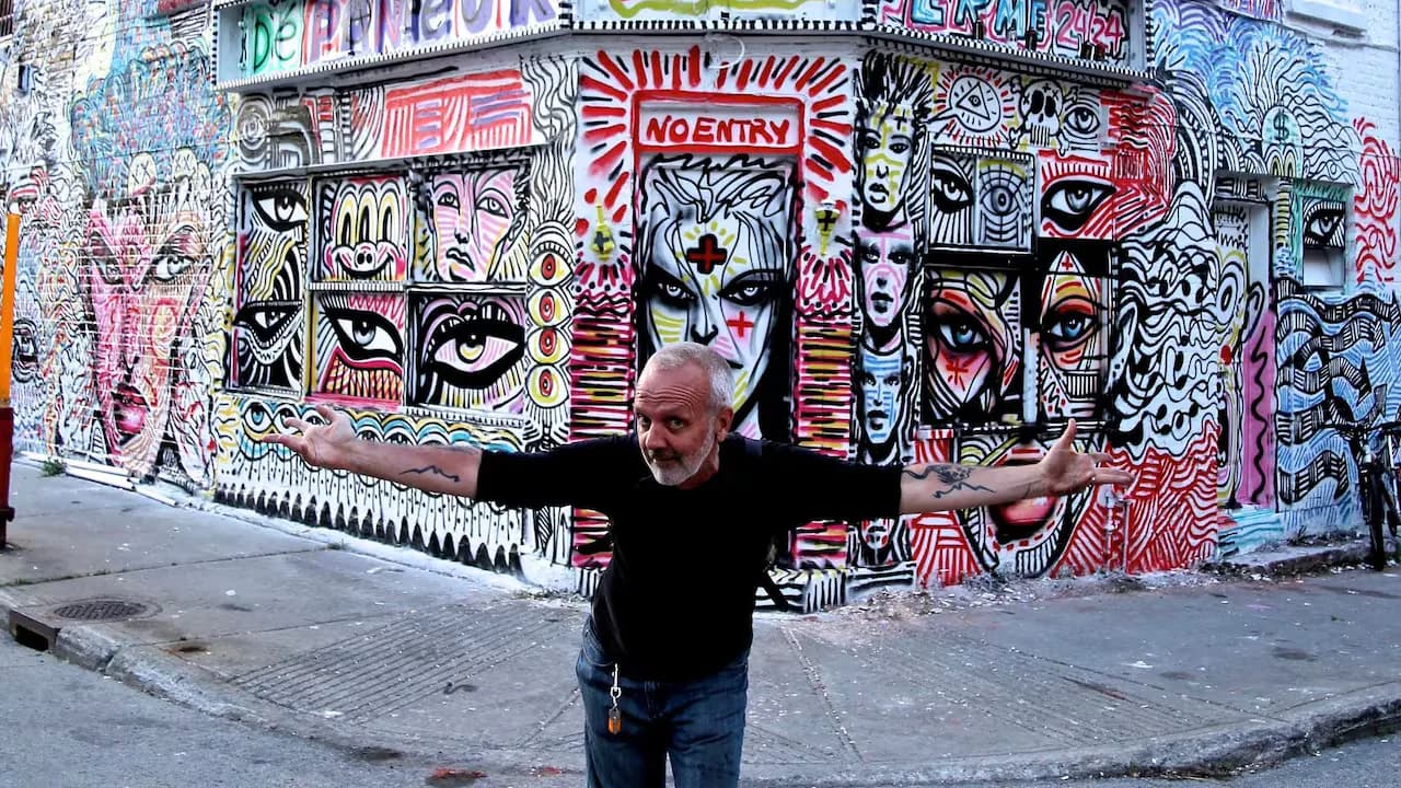 L'artiste Zilon, bras écartés devant l'une de ses murales de street art à Montréal