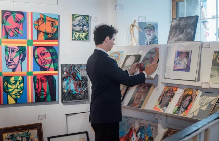 Dorian Verdier accroche une œuvre dans la galerie L'Original, entouré de tableaux d'artistes montréalais