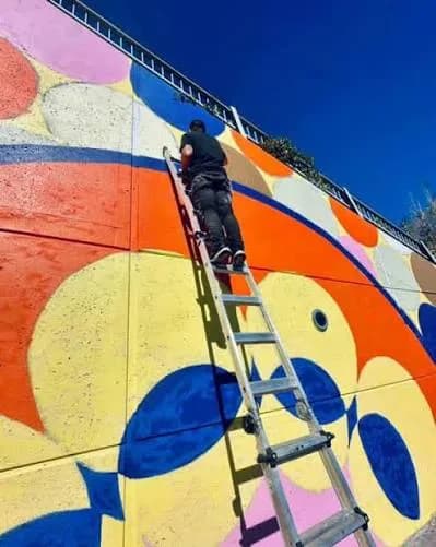 A muralist paints the “Fierté” mural on an outdoor wall in Montréal-Nord, working from a ladder