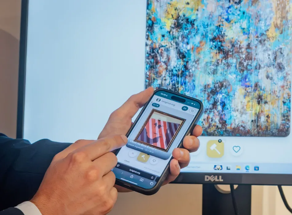 Une personne fait défiler les œuvres de PickArt sur son téléphone, devant une toile accrochée dans un bureau