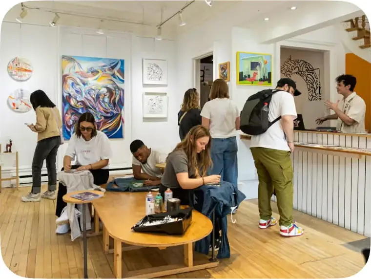 Visitors painting around the gallery's large wooden table during an evening.